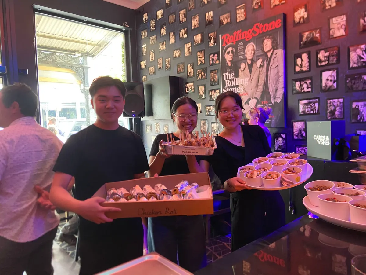 Mister Minh staff holding boxes of chicken roti, pork dim sims and noodle cups at a catered event